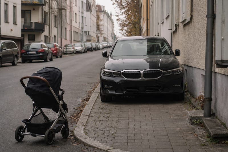 Pkw blockiert einen Gehweg, eine Person mit Kinderwagen muss auf die Fahrbahn ausweichen