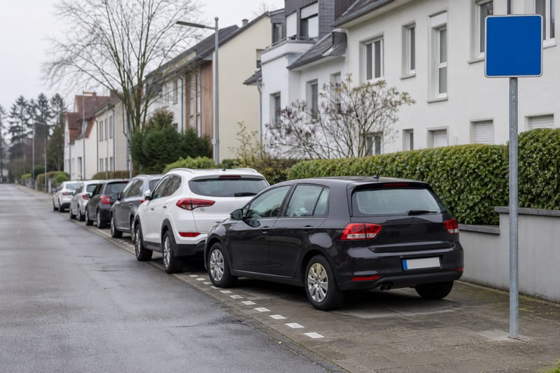 Fahrzeuge parken geordnet mit zwei Rädern auf einem markierten Gehwegstreifen, Zeichen 315 am Straßenrand